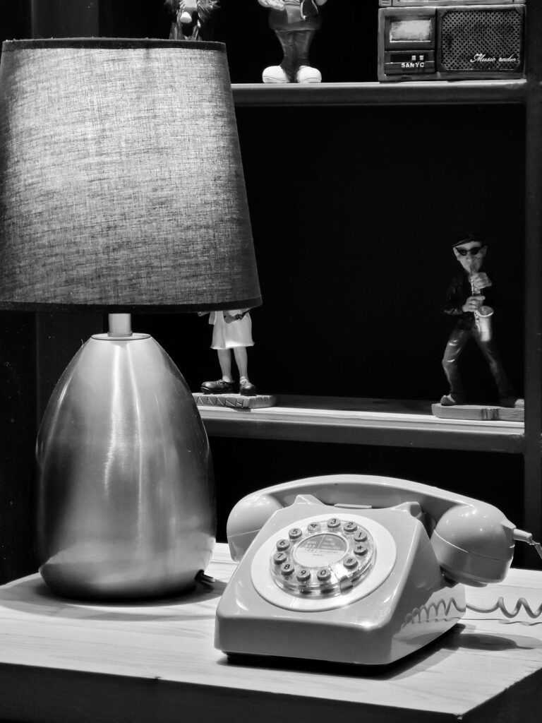 An old style telephone sitting on a hall bench under a liamp