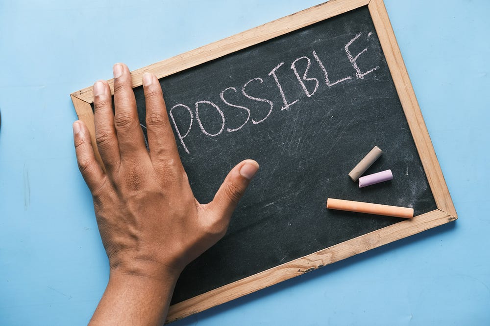 chalk board spelling the word "Impossible" with and hand covering the first two letters to make it possible.