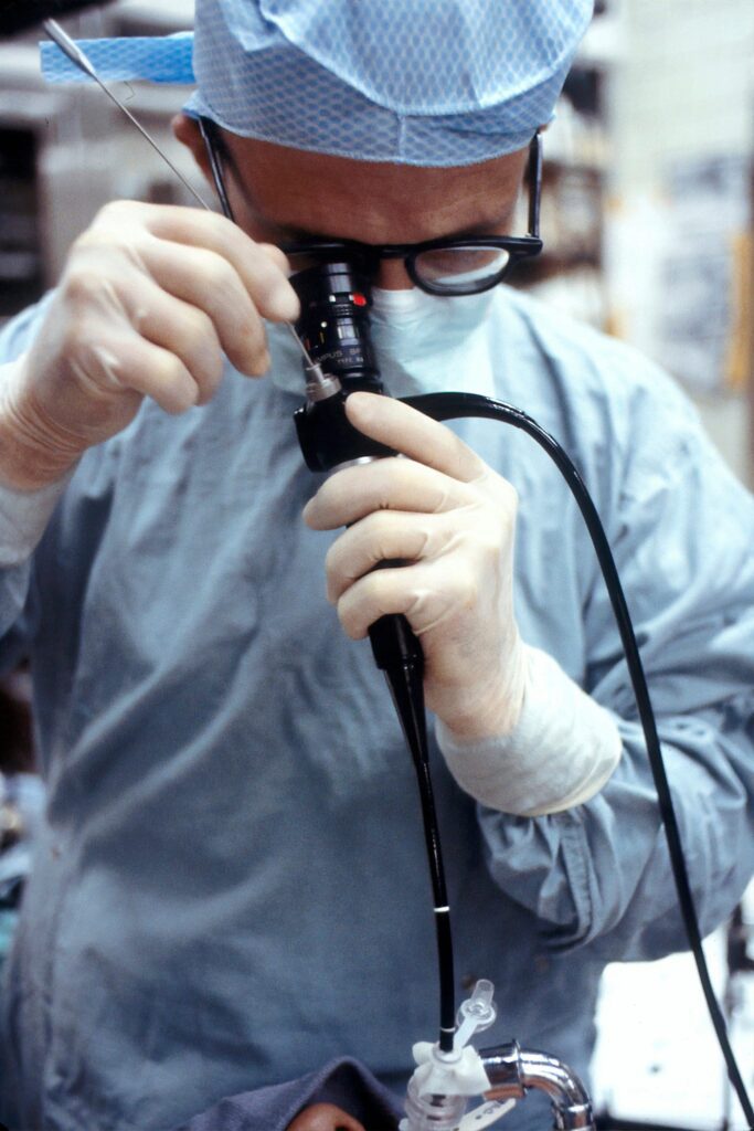 A surgeon in blue surgical scrubs looking down a telescopic camera during surgery